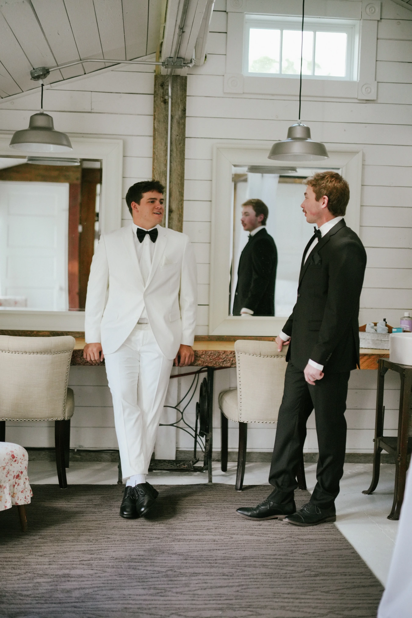 Teddy in his white suit teddysman black suit indoor conversation at Amy and Teddy's North Dakota farm wedding by Megaset Weddings