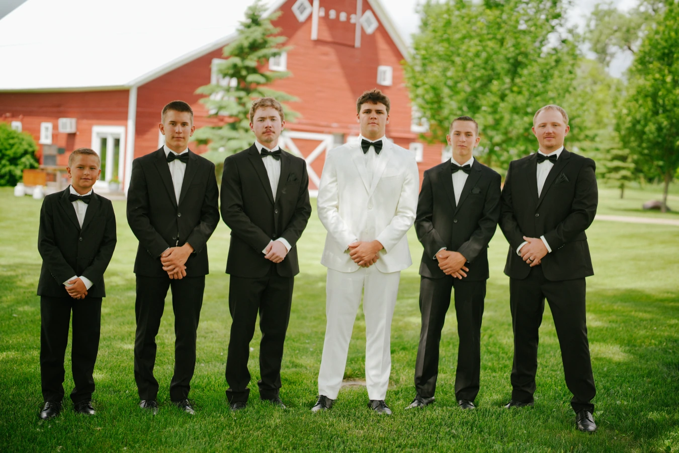 Teddy in his white suit teddysmen black suits rustic barn portrait at Amy and Teddy's North Dakota farm wedding by Megaset Weddings