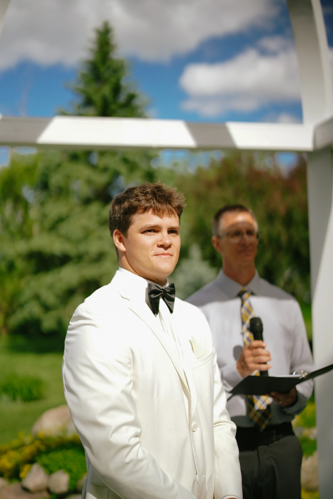 Teddy in his white suit ceremony arch at Amy and Teddy's North Dakota farm wedding by Megaset Weddings
