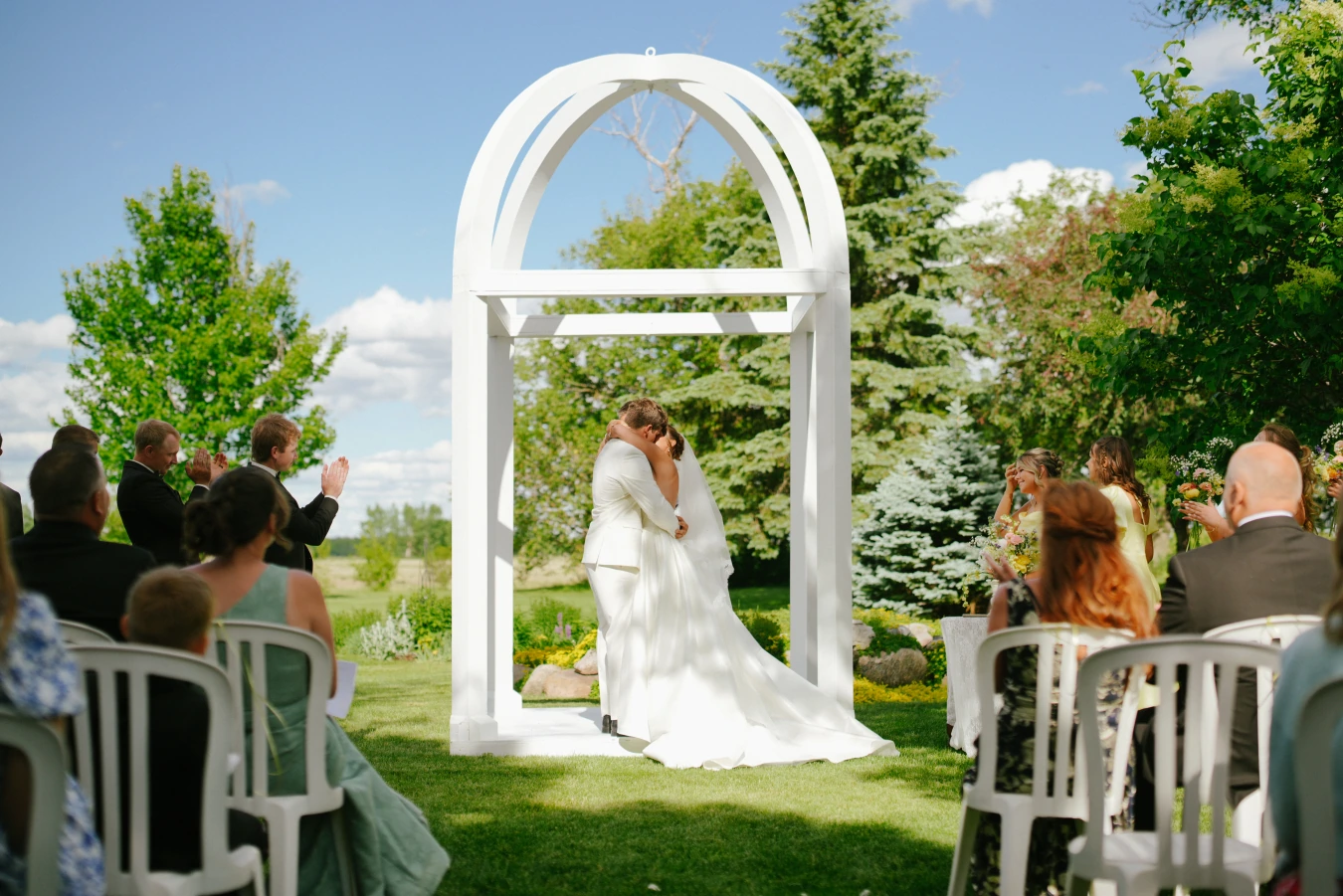 Outdoor arch kiss at Amy and Teddy's North Dakota farm wedding by Megaset Weddings