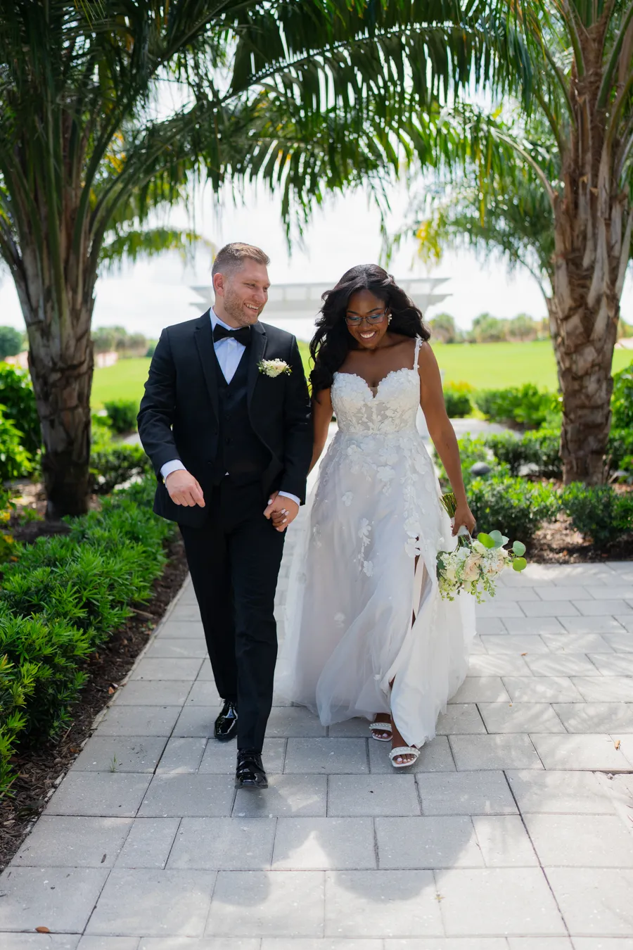 Newlyweds walking along a palm-lined path at The Club at Quail Ridge